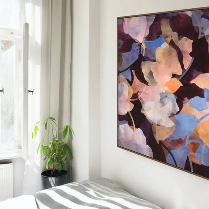 Abstract painting on a wall above a bed with a plant beside a window.