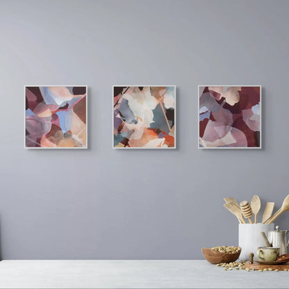 Three abstract art prints on a gray wall above a white surface with kitchen items.