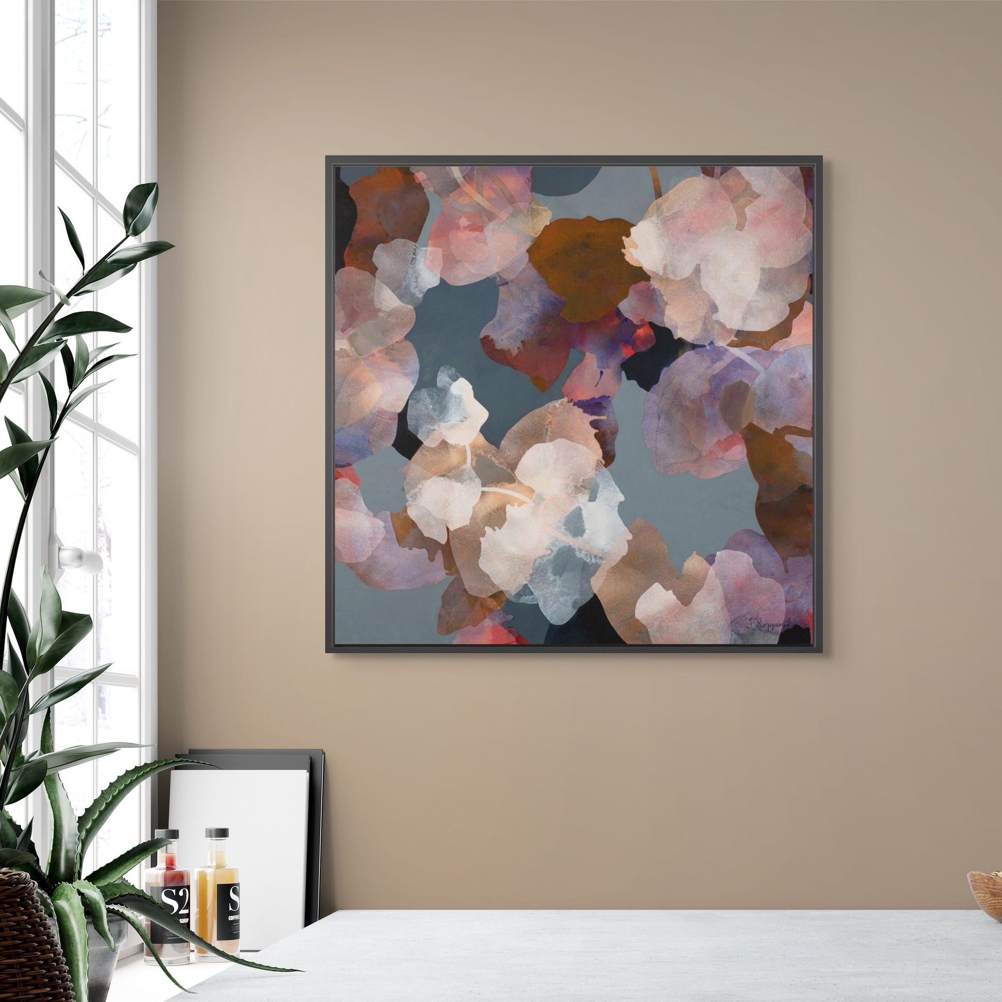 Framed abstract floral colorful art on a beige wall with a plant and window.