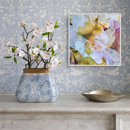 Decorative vase with flowers on a table against a patterned wall with a framed abstract painting.