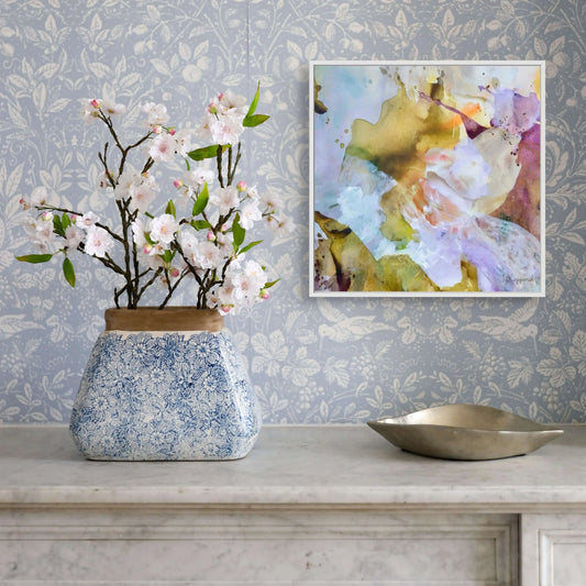 Decorative vase with flowers on a table against a patterned wall with a framed abstract painting.